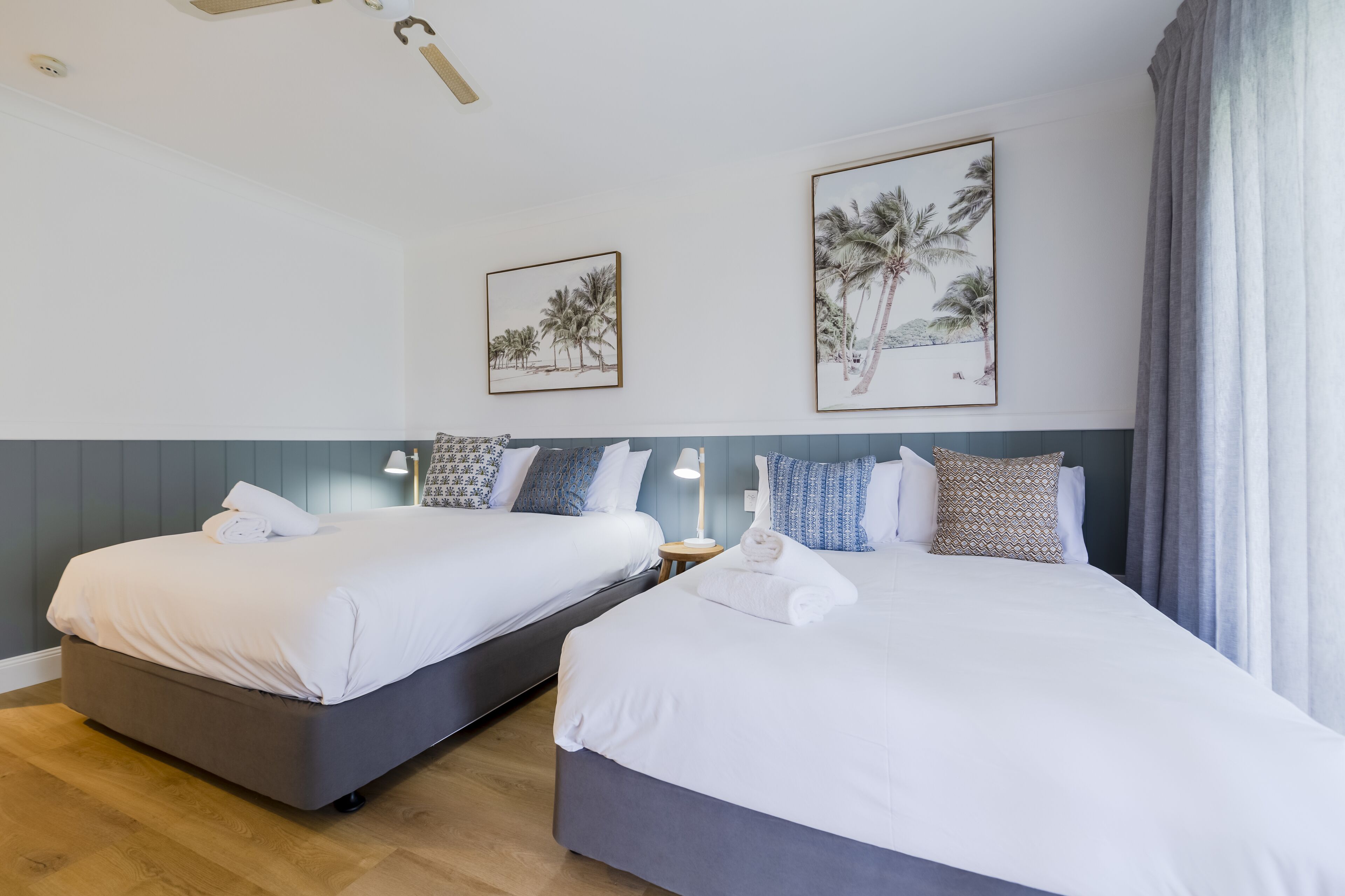 Une chambre d’hôtel avec deux lits, une table de chevet et une lampe. Deux tableaux encadrés sont accrochés au mur.
