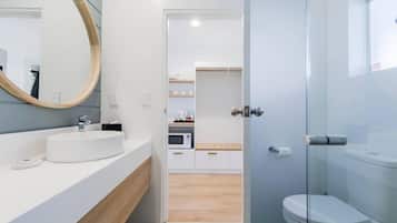 Uma casa de banho moderna com cabine de duche em vidro, uma sanita e uma pia branca com espelho redondo.