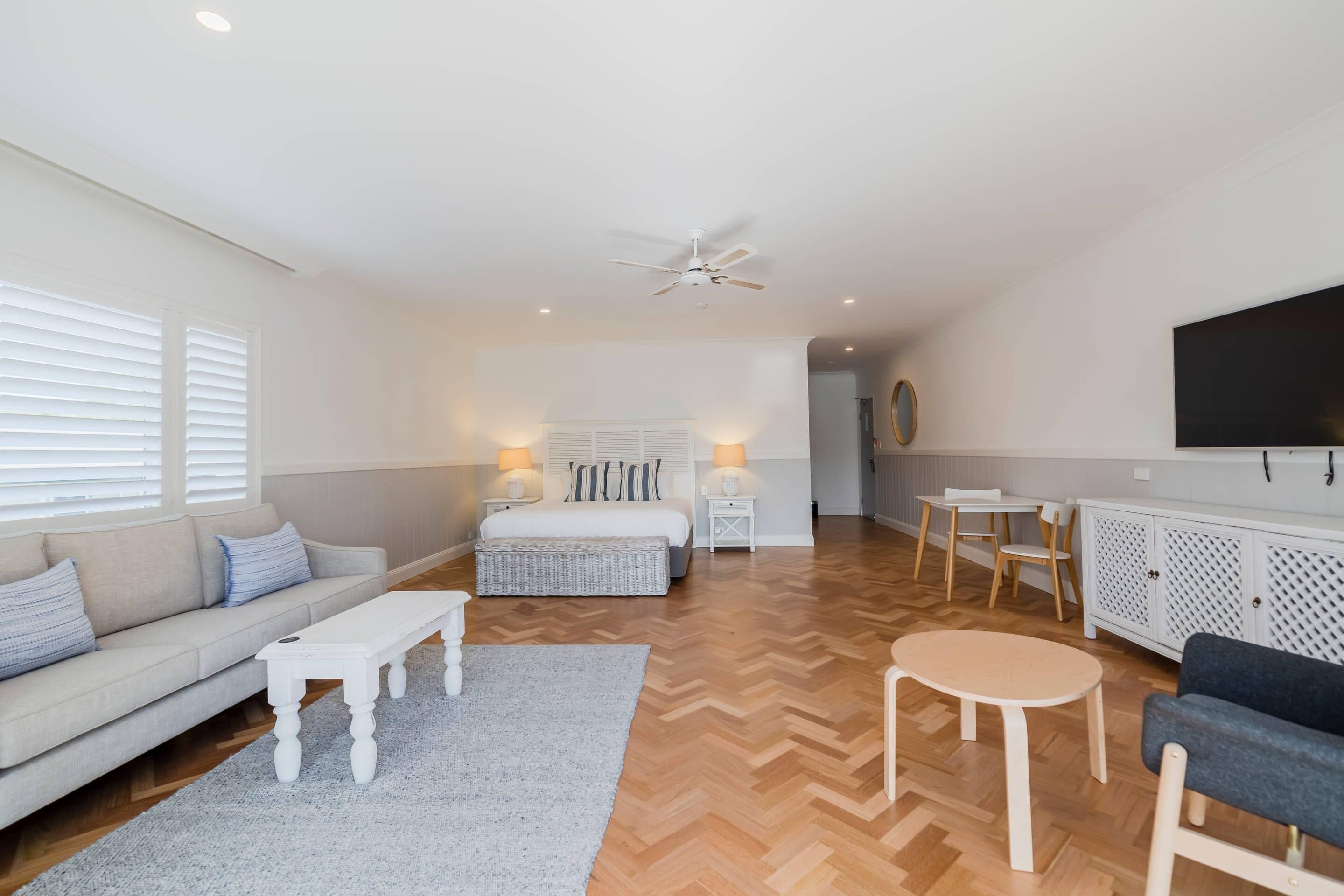 A spacious room with a large bed, a sofa, a coffee table, a TV, and a ceiling fan.