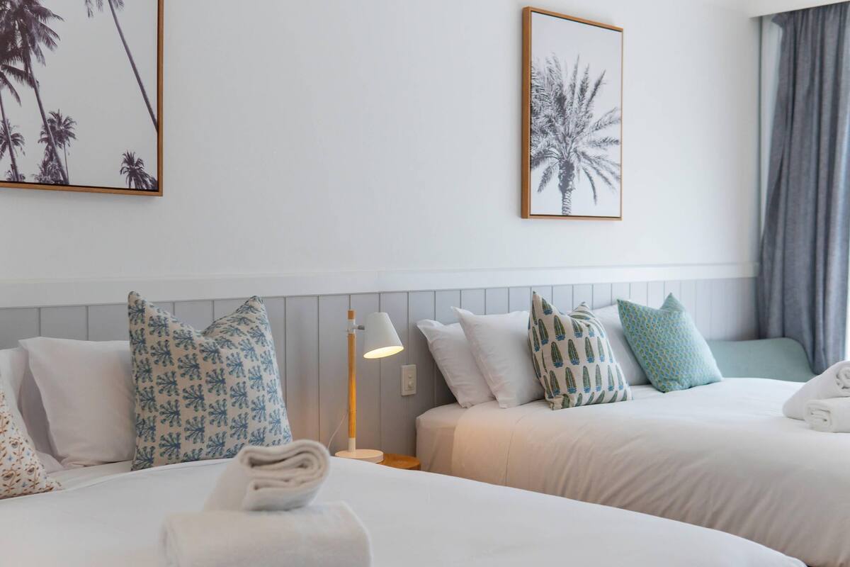 A hotel room with two beds, a nightstand, a lamp, and framed artwork on the walls.