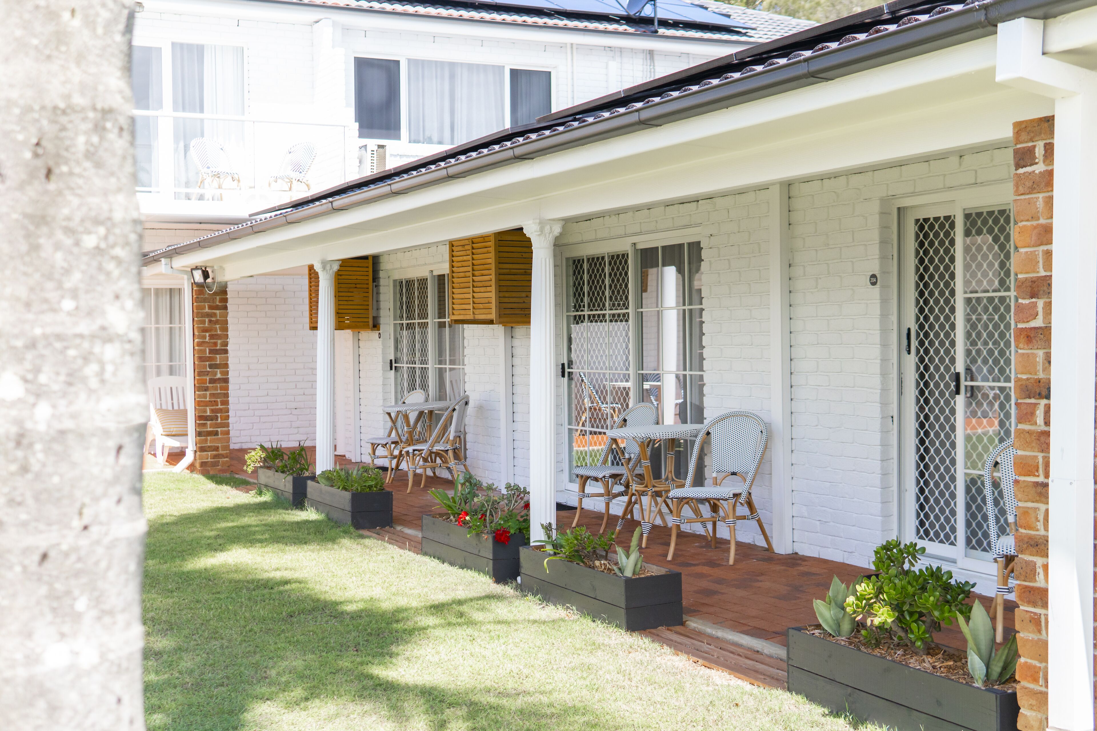 A white brick house with a covered porch, outdoor seating, and potted plants.