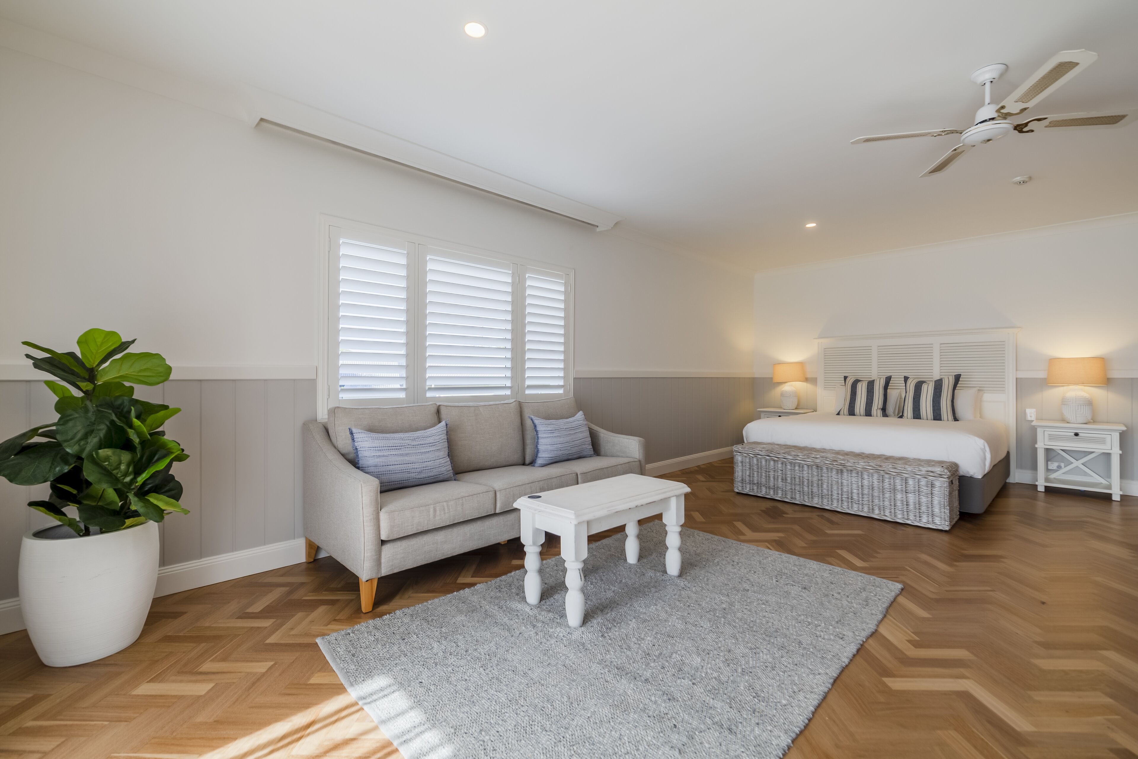 A modern bedroom with a bed, a sofa, a coffee table, and a potted plant.
