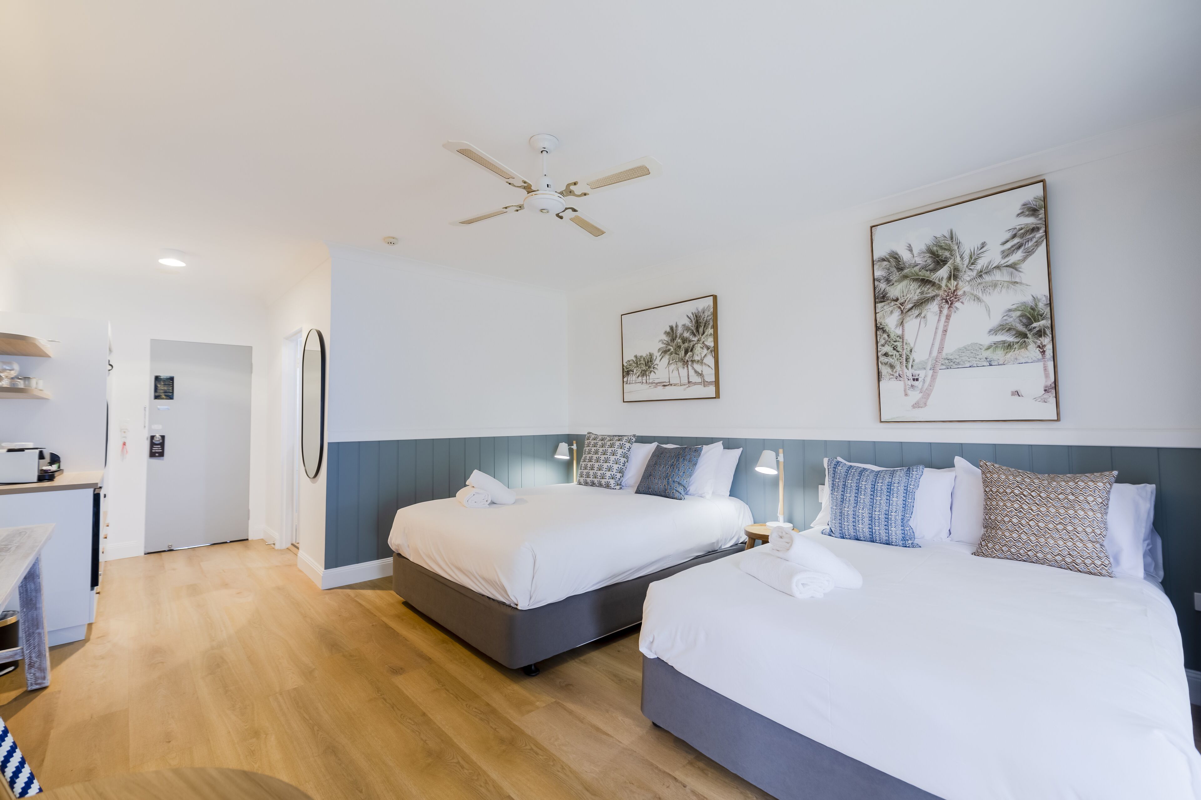 Habitación de hotel con dos camas, ventilador de techo y obras de arte en las paredes.
