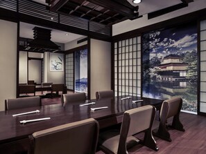 Une salle de conférence dotée d’une grande table, de chaises et offrant une vue sur un bâtiment japonais traditionnel, visible à travers une porte coulissante.