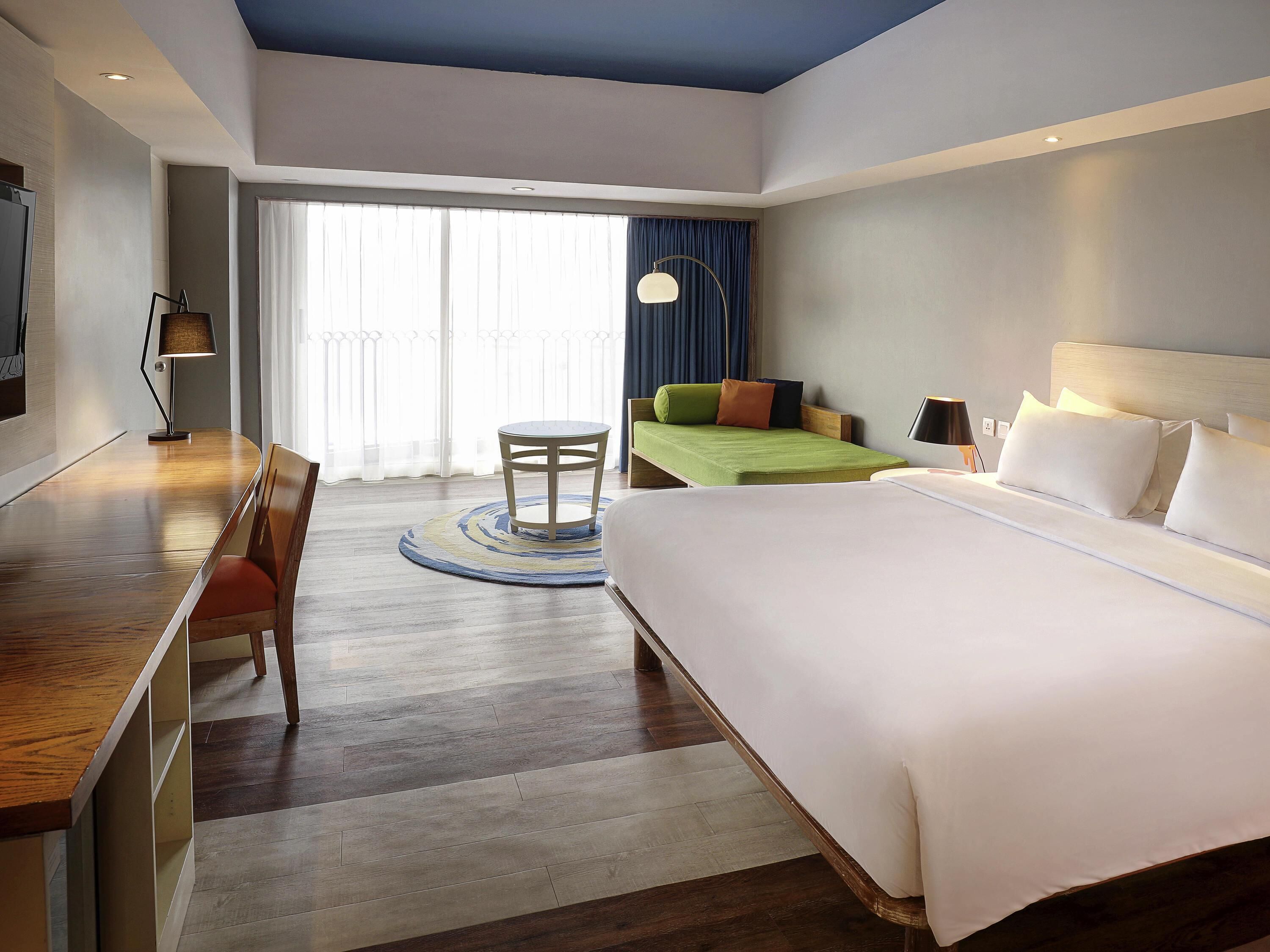 A hotel room with a bed, a desk, a chair, a round table, and a large window with curtains.