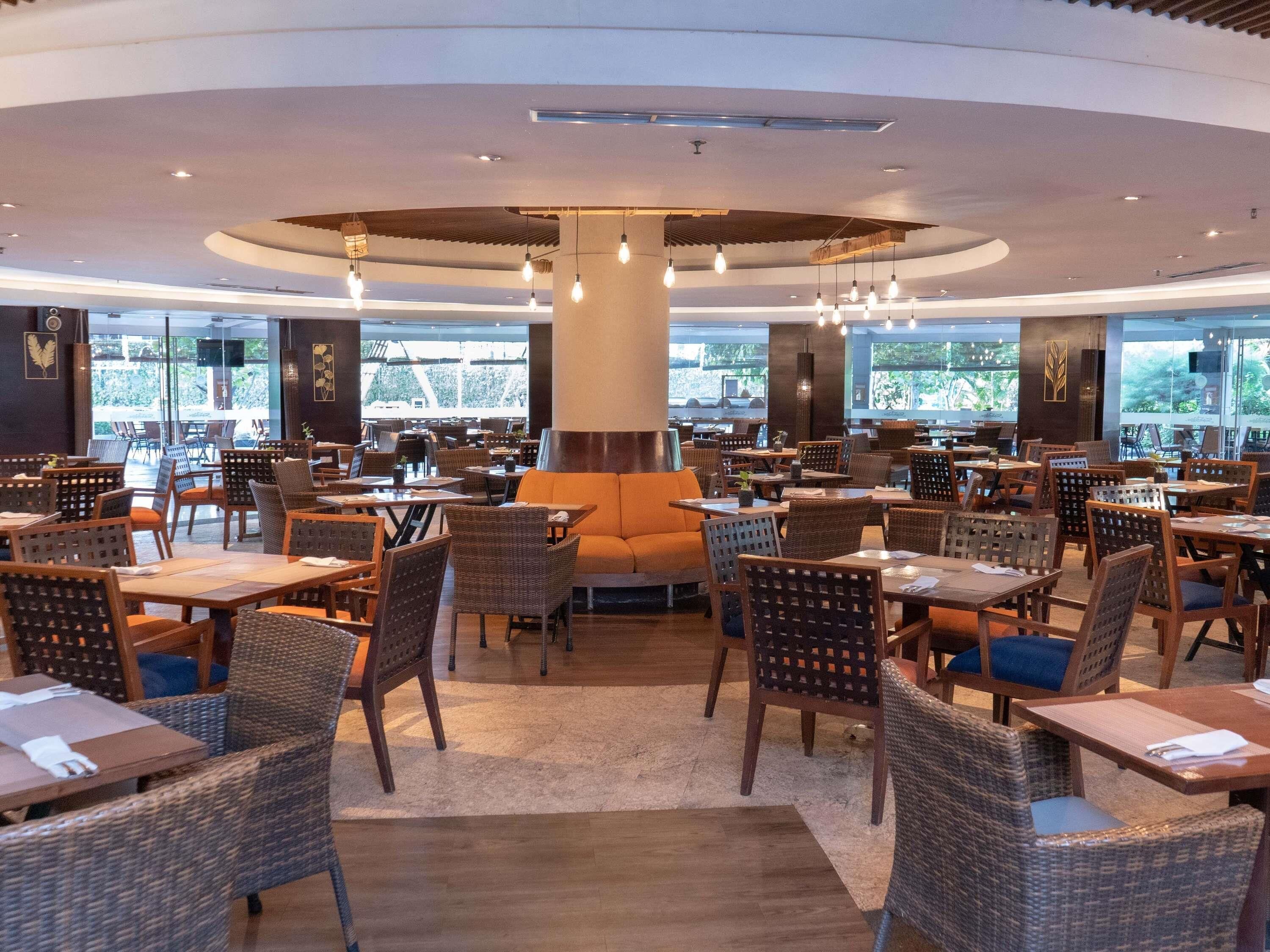 Un restaurante espacioso con techos altos, mobiliario de mimbre y amplios ventanales que ofrecen una vista.