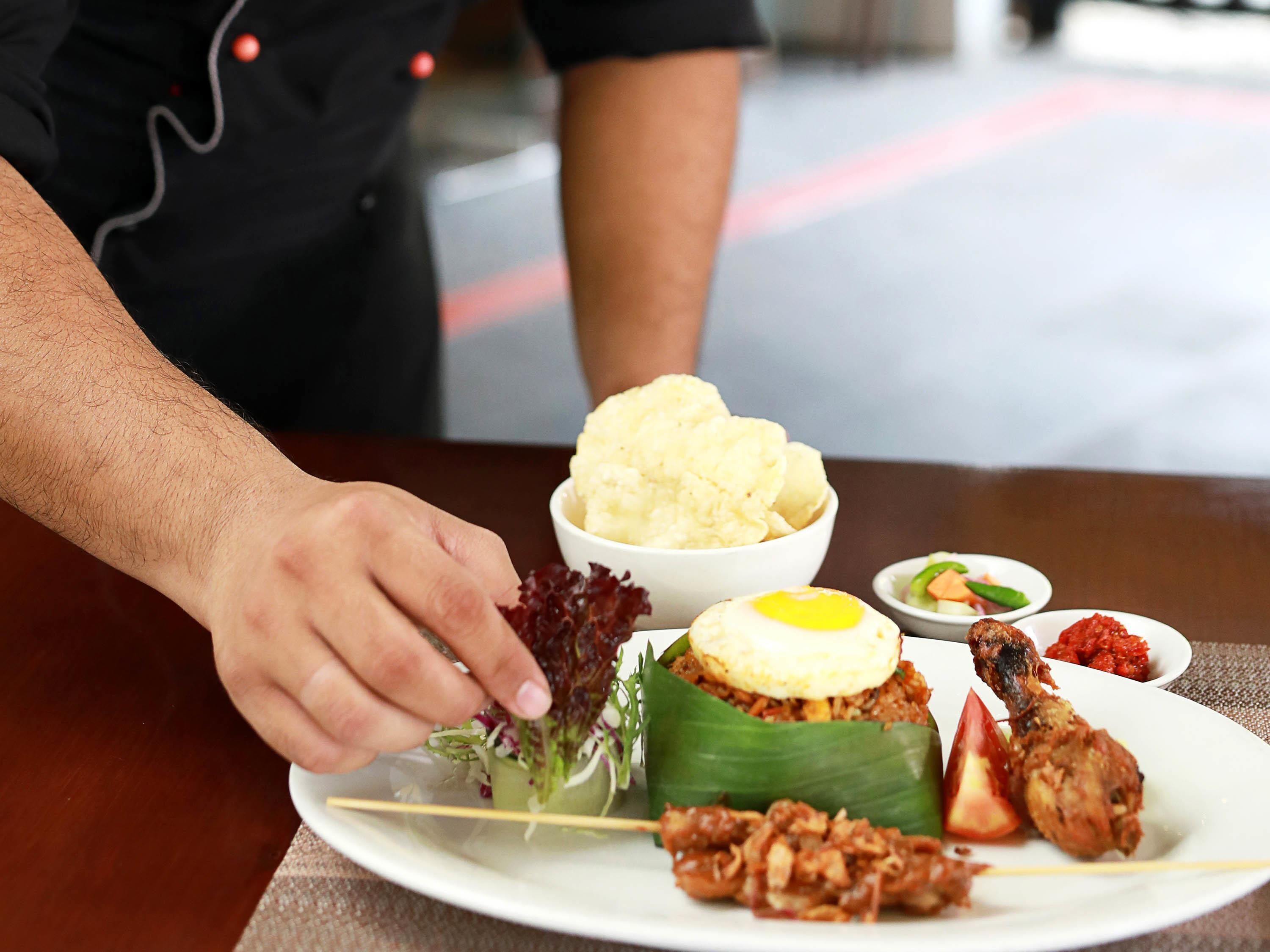 Une assiette contenant divers plats, notamment un œuf frit, un wrap aux légumes et une portion de sambal.