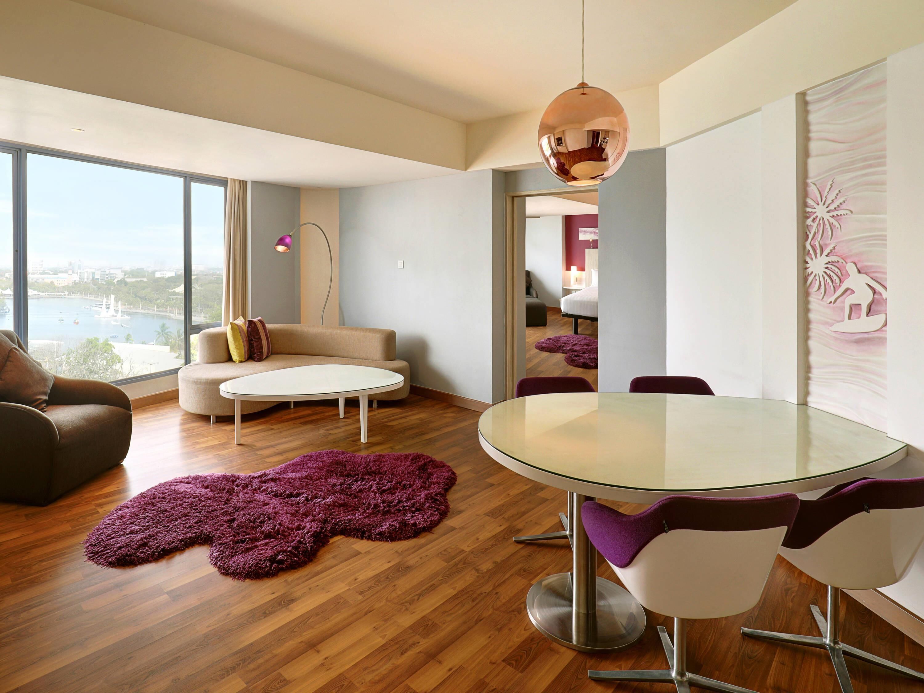 Ein modernes Wohnzimmer mit einem Glastisch, violetten Stühlen, einer Couch und Blick auf die Stadt.