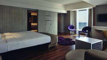 Una habitación de hotel moderna con una cama grande, un área de descanso con dos sillones, una mesita y un televisor.