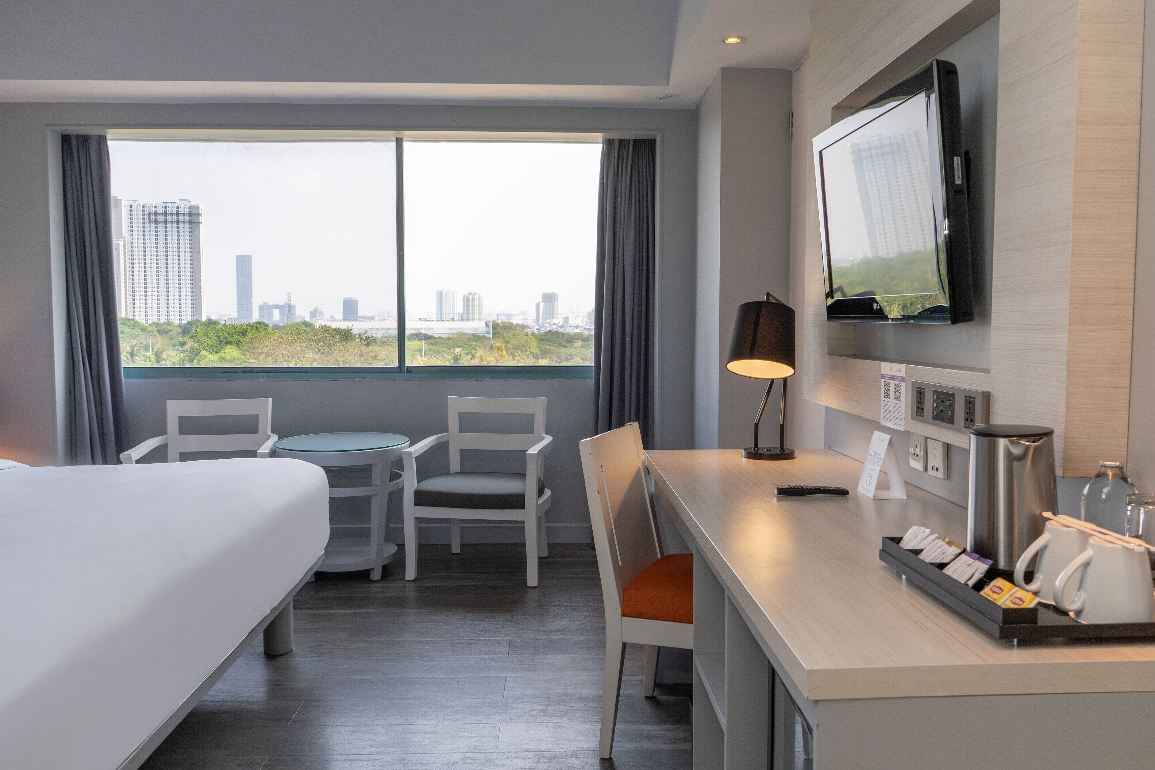 Hotelkamer met een bed, een bureau met koffiezetapparaat, een televisie en uitzicht over de stad.