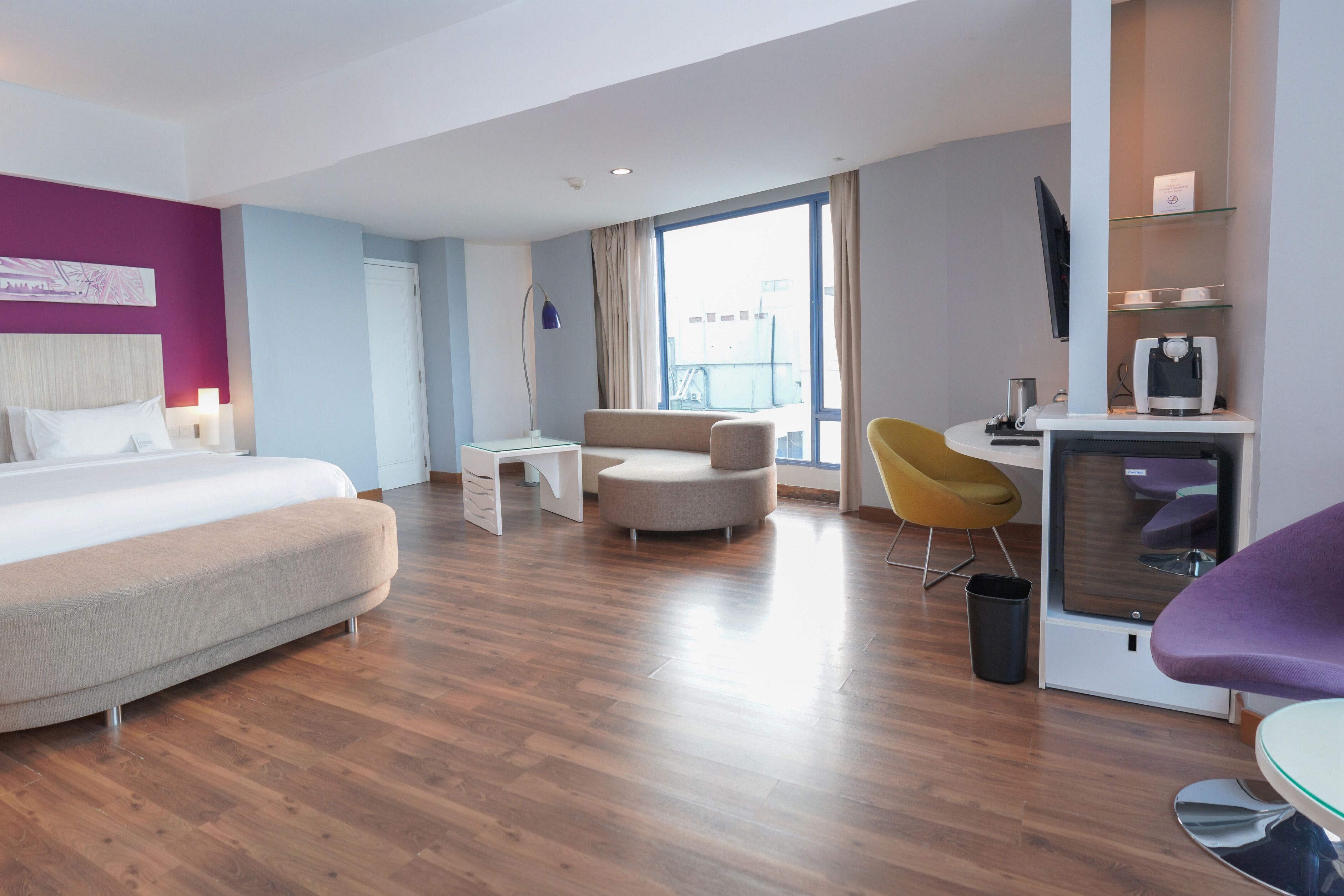 Habitación de hotel con cama, escritorio, sofá, sillón, televisión y cafetera.