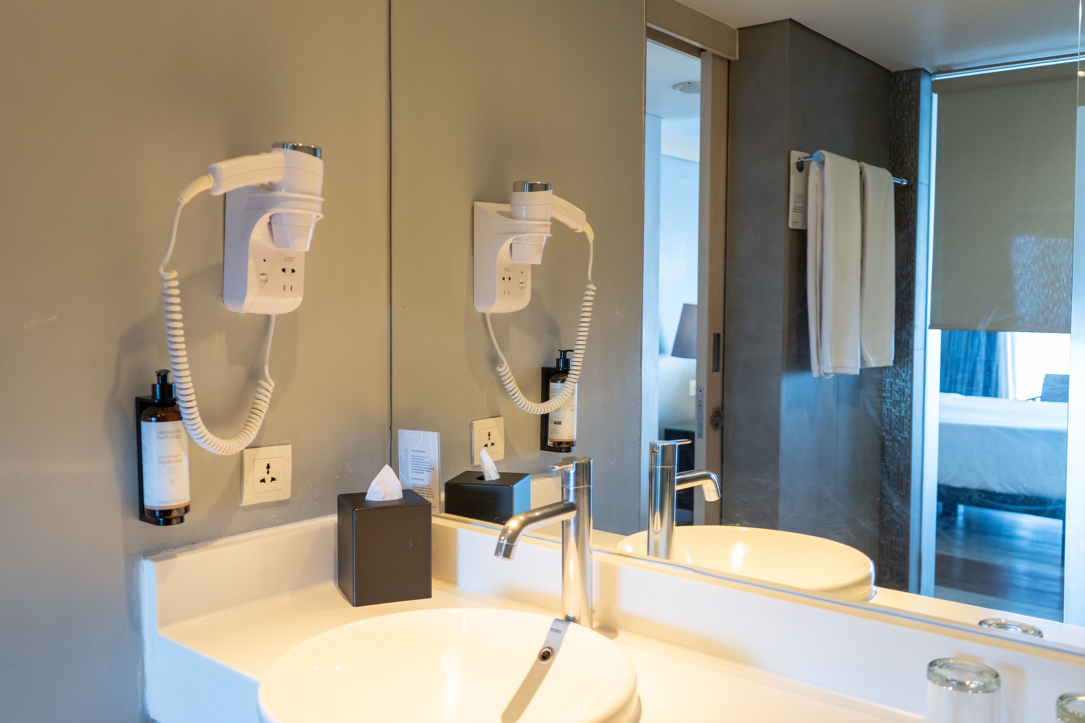 A bathroom with a sink, mirror, and hairdryer mounted on the wall.