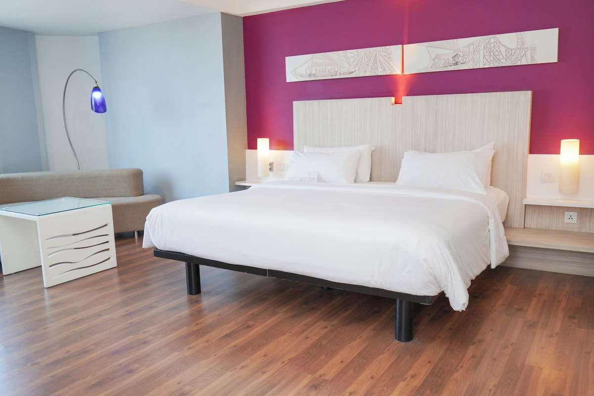 A modern hotel room with a large bed, a small sofa, and a desk.