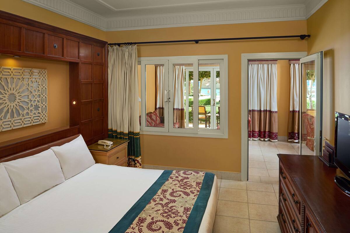 Een hotelkamer met een groot bed, een houten dressoir, een bureau met telefoon en een raam met gordijnen.