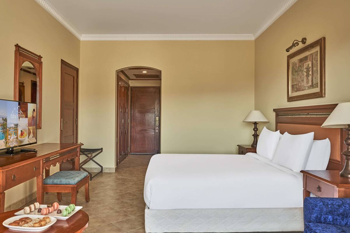 Een hotelkamer met een bed, een bureau met stoel, een televisie en een eettafel met gebak.
