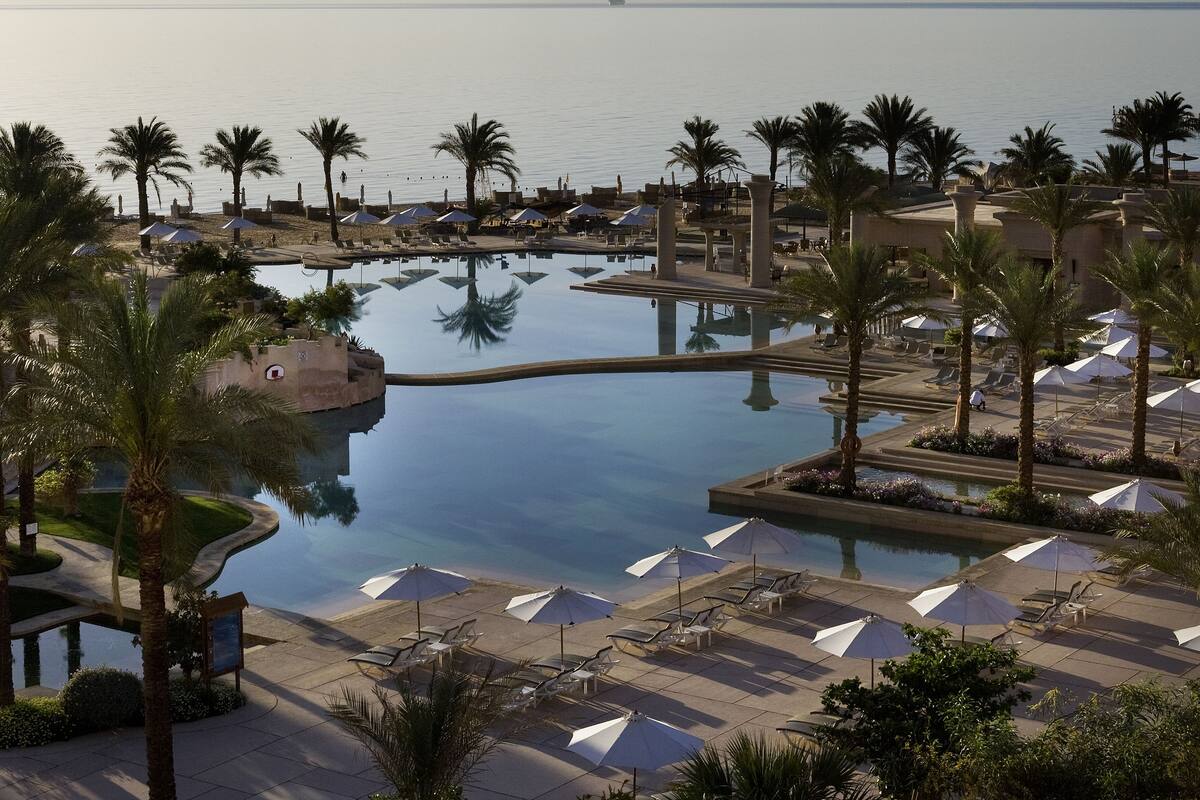 Een resort met een groot zwembad, palmbomen en uitzicht op de zee.
