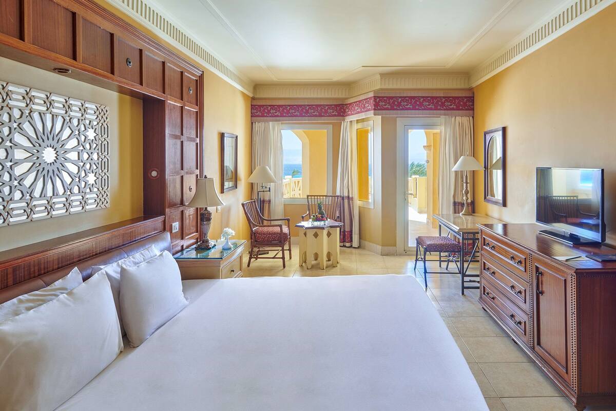 Een hotelkamer met een groot bed, een bureau, een televisie en uitzicht op de oceaan.