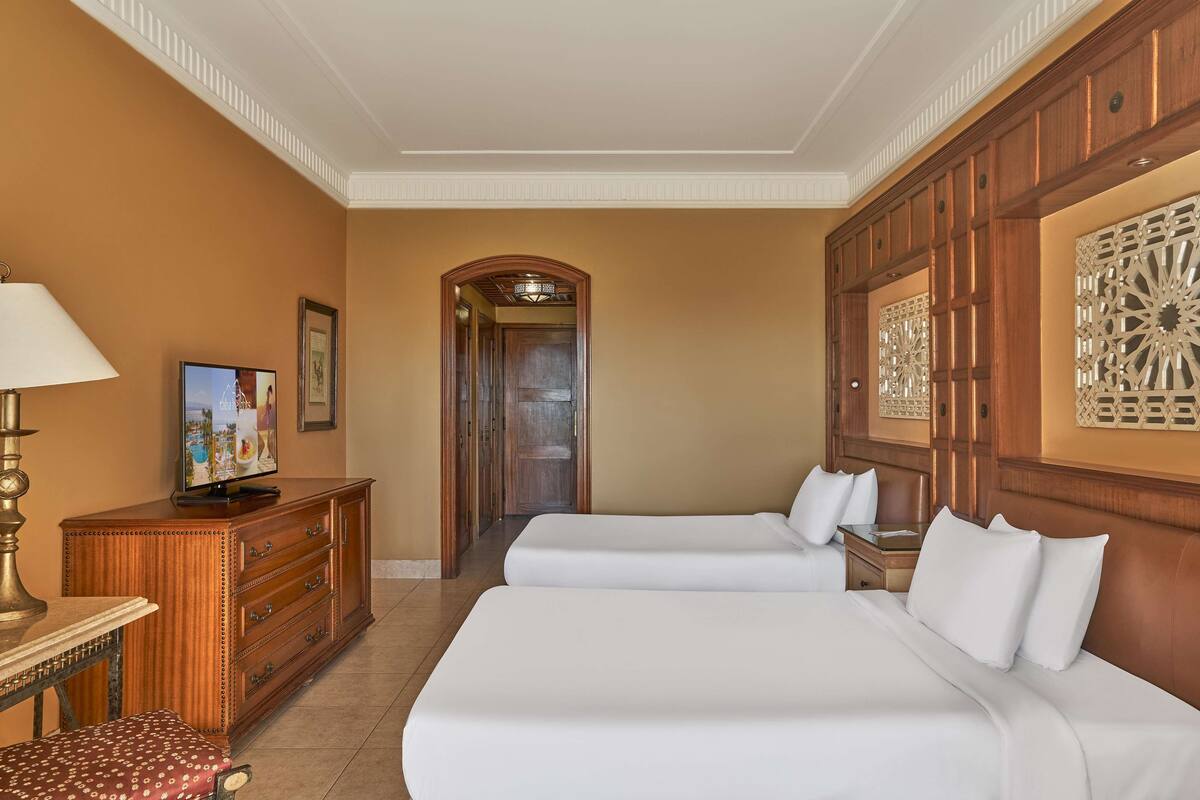 Een hotelkamer met twee bedden, een televisie, een bureau en een decoratief kunstwerk aan de muur.