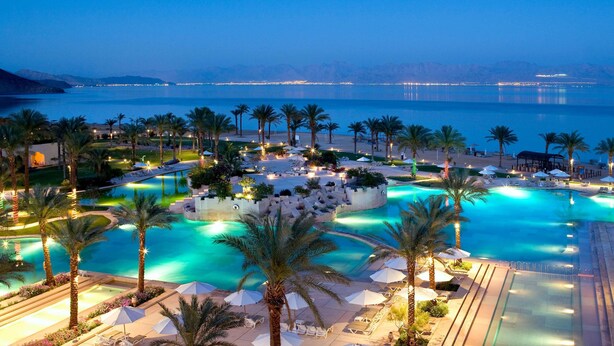 Ein Resort mit großem Schwimmbad, Palmen und Meerblick.