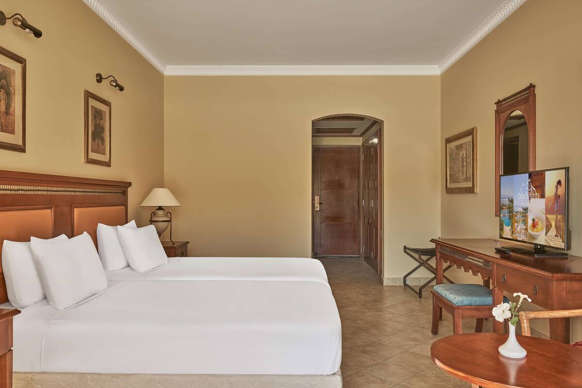 Een hotelkamer met een groot bed, een bureau met stoel, een televisie en een deur naar een andere kamer.