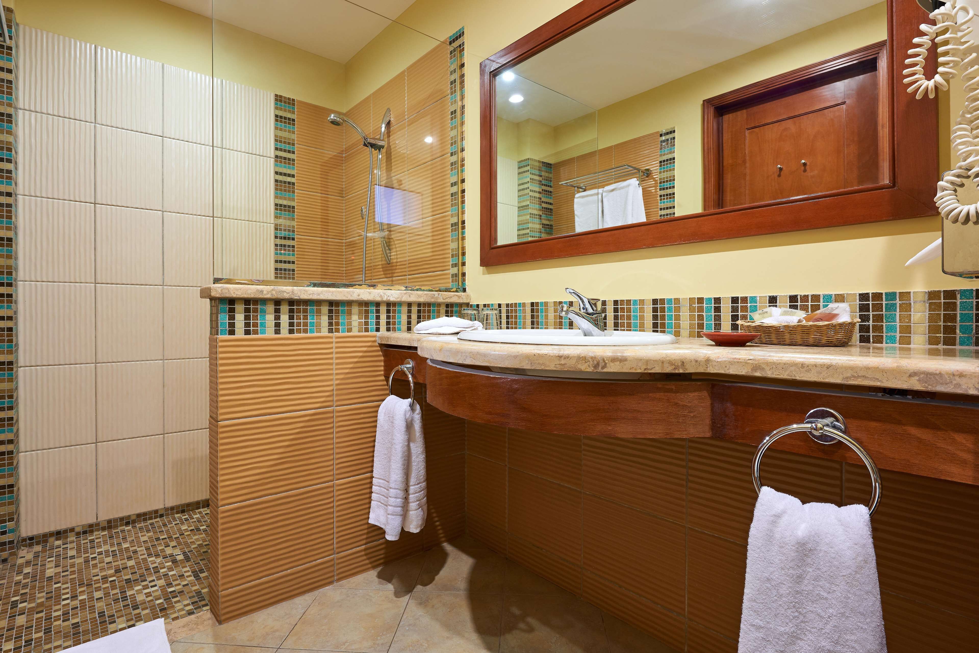 A bathroom with a large mirror, a shower, and a sink with a towel rack.