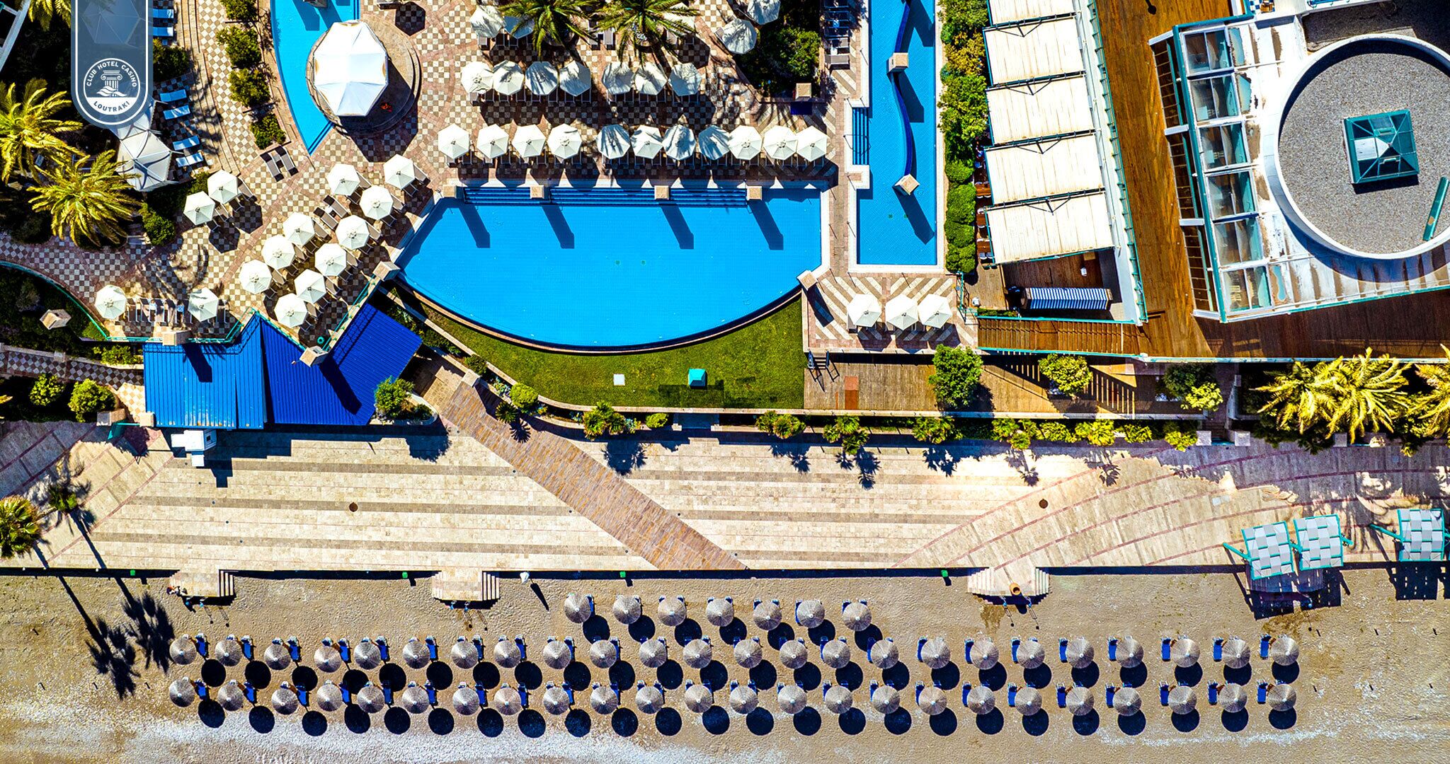 An aerial view of a hotel with a large pool, multiple lounge areas, and a staircase leading to a deck.