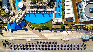 Vue aérienne d’un hôtel doté d’une grande piscine, de plusieurs espaces de détente et d’un escalier menant à une terrasse.