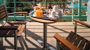 A balcony with a table set for breakfast, overlooking a beach and ocean.