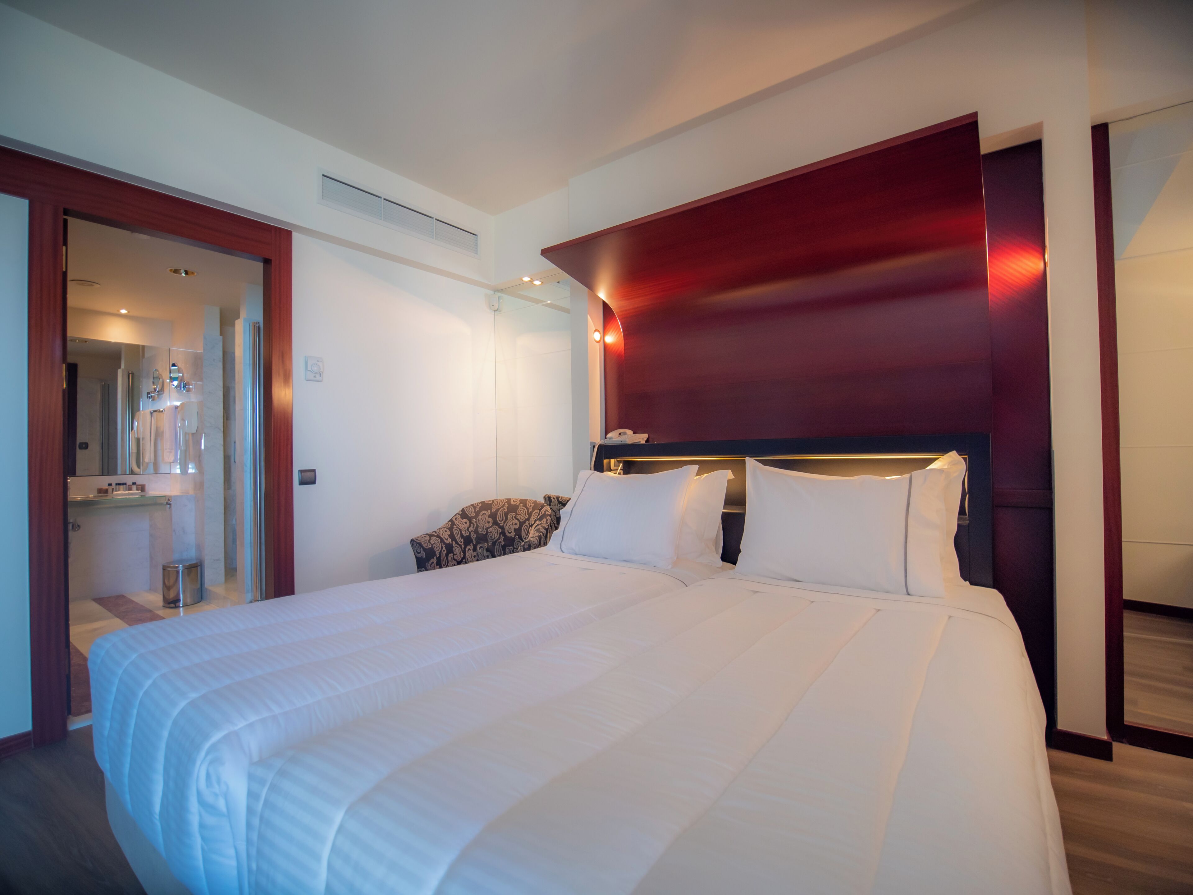 Habitación de hotel con una cama grande, un espejo, una tocador con lavabo y una puerta que da al baño.