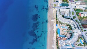 An aerial view of a coastal resort with a curved road, a central pool area, and a beach.