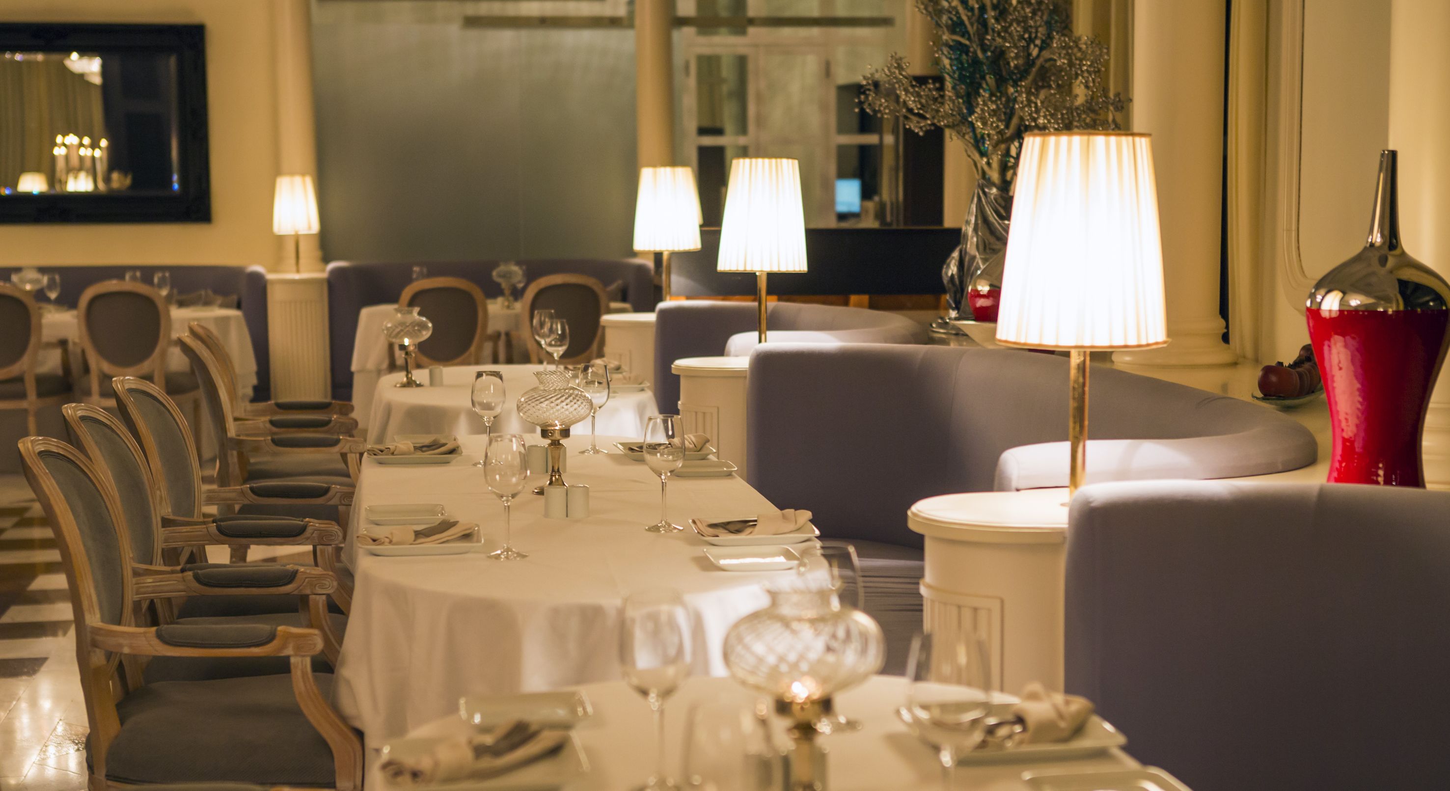 A formal dining room with round tables, chairs, and table settings including wine glasses and plates.