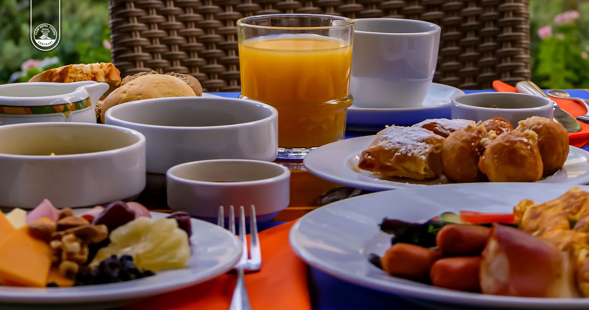 Una mesa de desayuno con diversos platos, entre ellos bollería, frutas y un vaso de zumo de naranja.