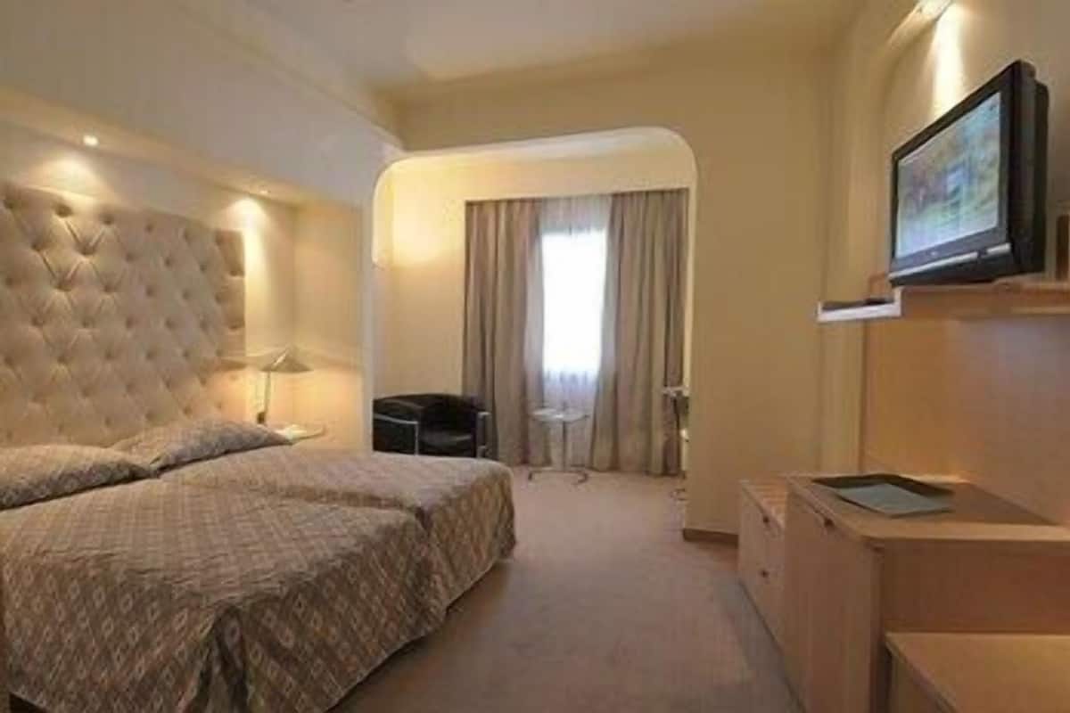Ein Hotelzimmer mit einem großen Bett, einem Schreibtisch, einem Stuhl, einem Fernseher und einem Fenster mit Vorhängen.