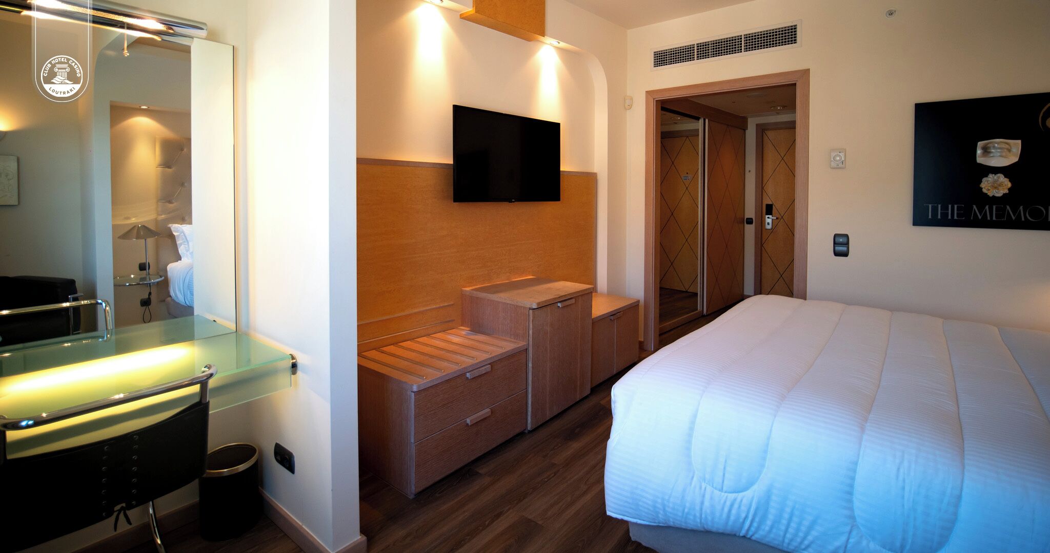 Una habitación de hotel con cama, televisión montada en la pared, un armario de madera y un espejo.