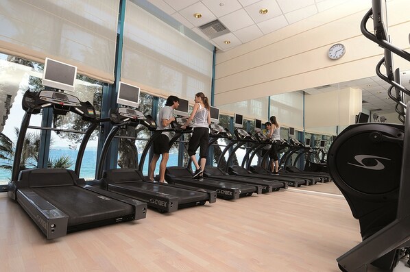 Une salle de sport équipée de tapis de course, d’appareils d’exercice et de grandes fenêtres donnant sur un plan d’eau.