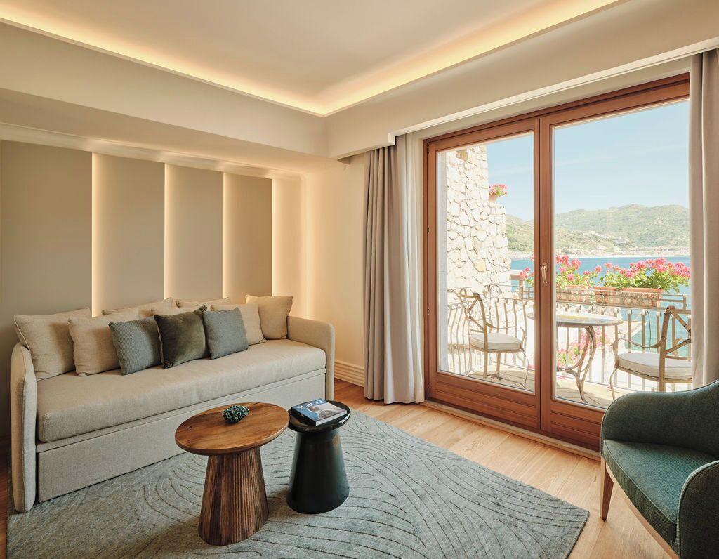 A living room with a sofa, a coffee table, and a view of a balcony with outdoor furniture.