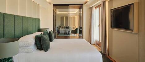 A hotel room with a bed, a TV, a desk with a lamp, and a view of the hallway.