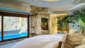 A bedroom with a large bed, a stone wall, and a view of a swimming pool.