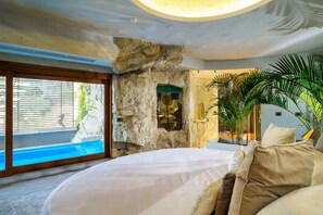 Quarto com cama grande, parede de pedra e vista para uma piscina.