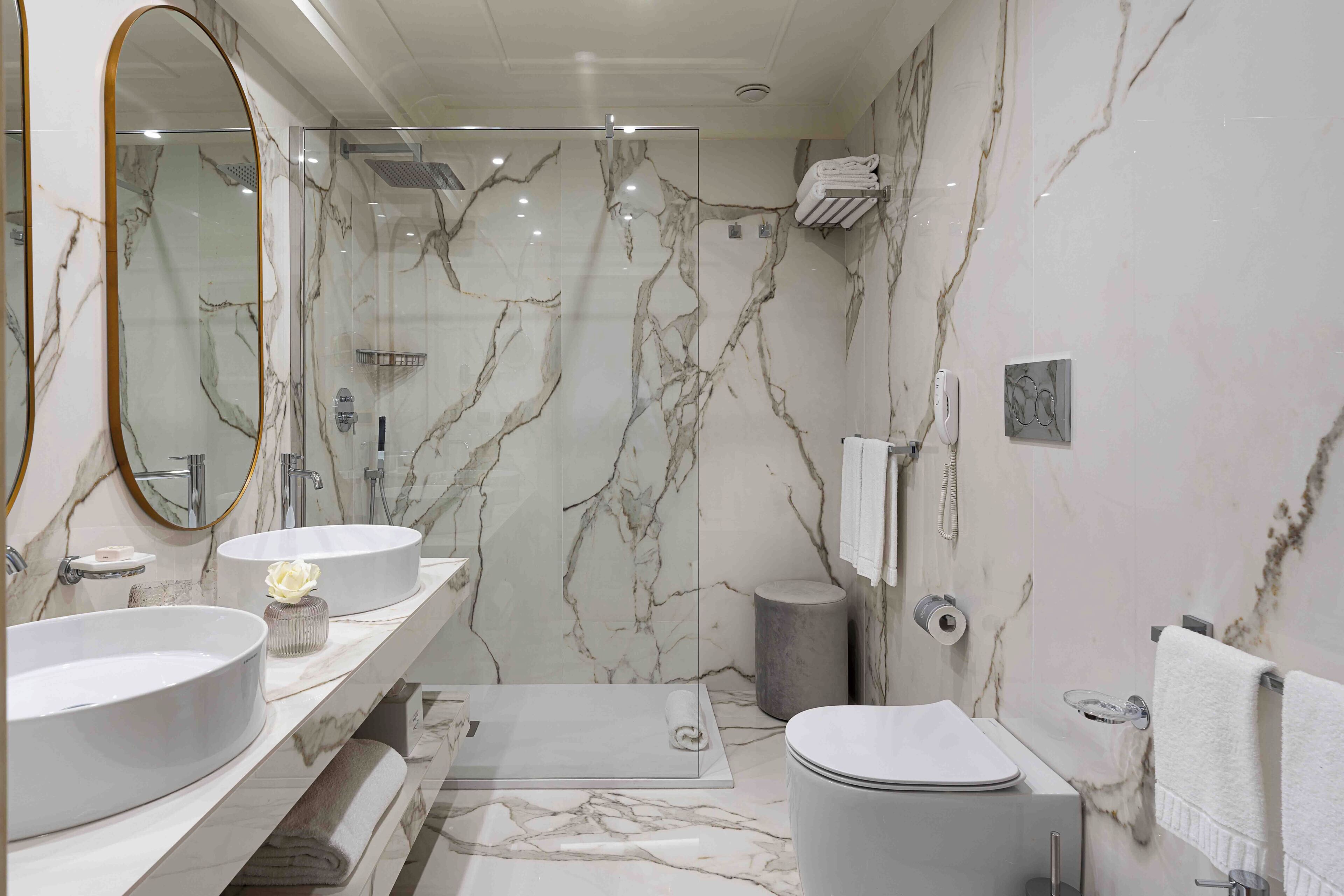 Un baño con dos lavamanos, un inodoro, ducha y paredes de mármol.