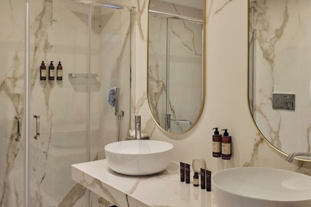 A bathroom with a marble wall, a round sink, a large mirror, and a shower enclosure.