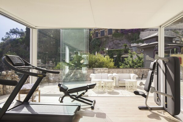 A modern outdoor gym with exercise equipment, a white outdoor seating area, and a view of a hillside with vegetation. - Atlantis Bay - The Leading Hotel of the World (Taormina)