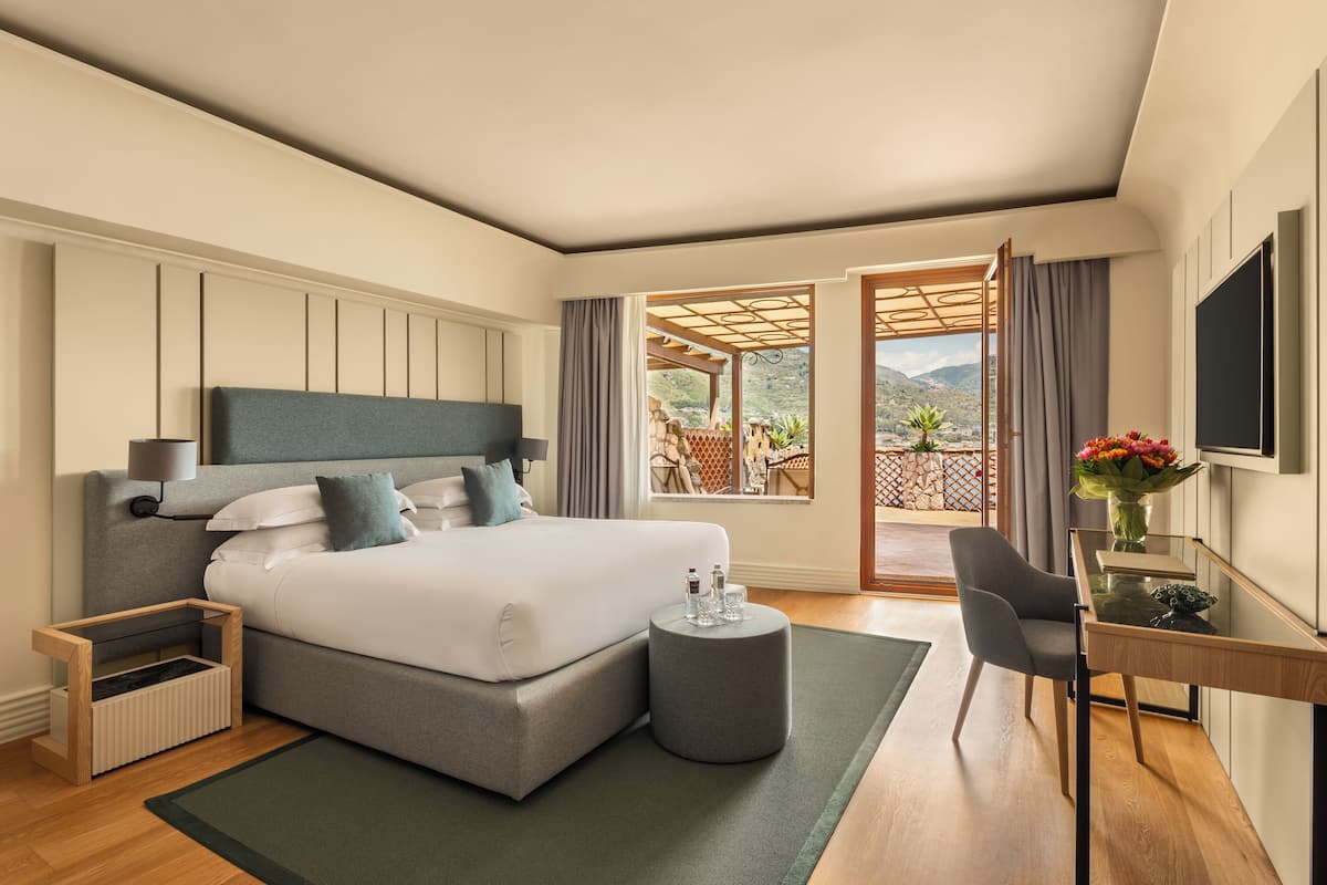 A modern bedroom with a large bed, a desk, and a view of the outdoors.
