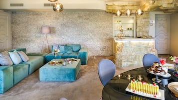 Un salon moderne avec un canapé, une table basse et un coin repas où l’on aperçoit un gâteau et des verres.