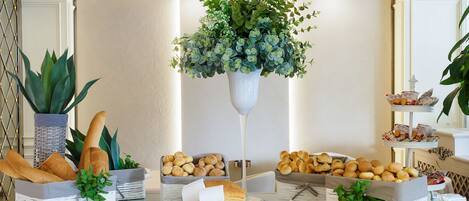 A buffet setup with various breads and pastries, a cutting board with a knife, and a hanging plant.