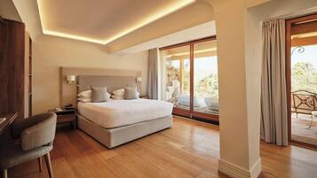 Une chambre spacieuse avec un grand lit, des tables de chevet, un fauteuil et une vue sur l’extérieur grâce à une porte-fenêtre coulissante.