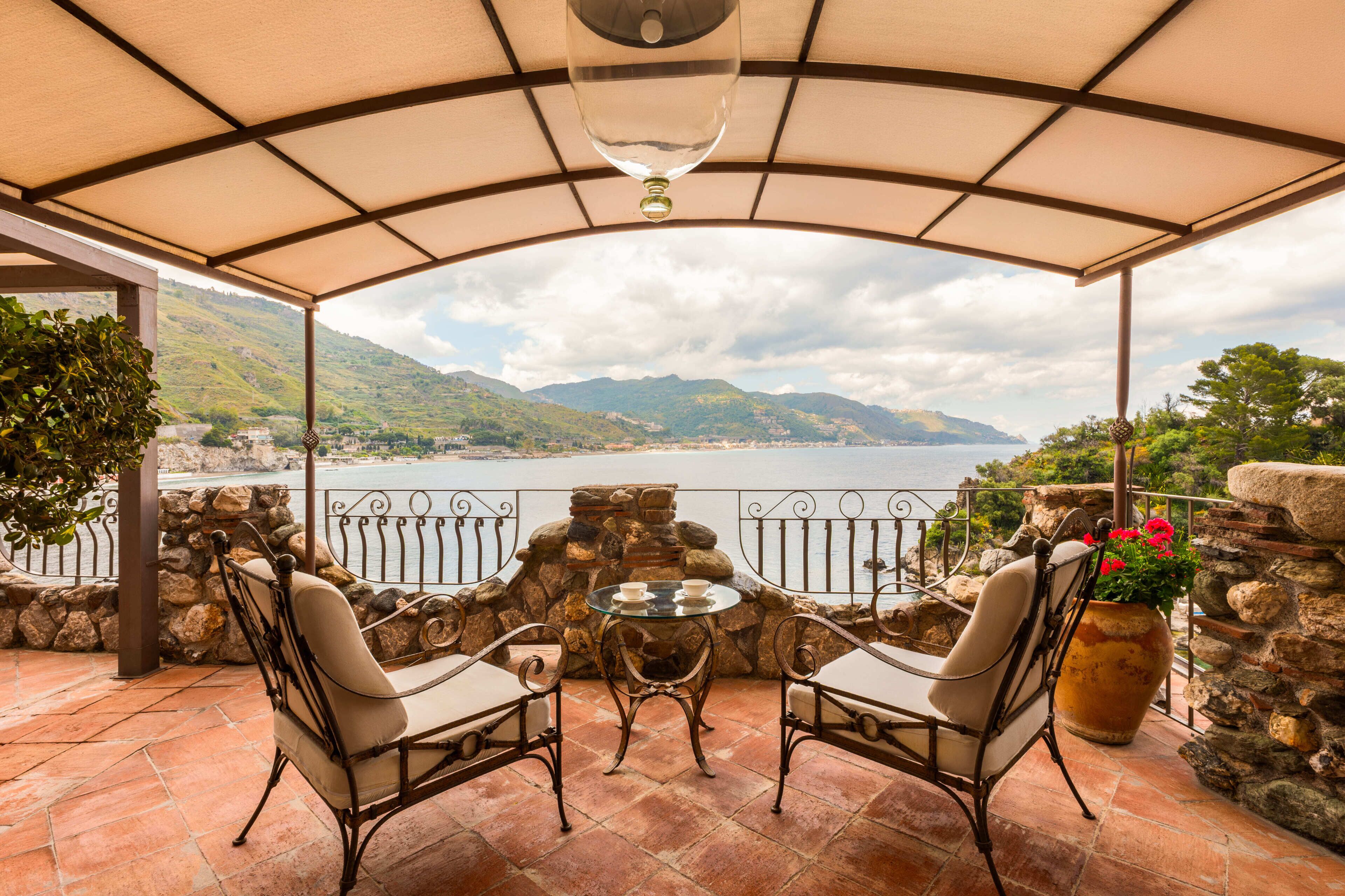 A covered patio with two chairs and a table, overlooking a lake and mountains.