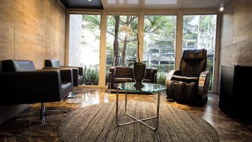 Een modern interieur met een massagestoel, een glazen tafel en uitzicht op groen.