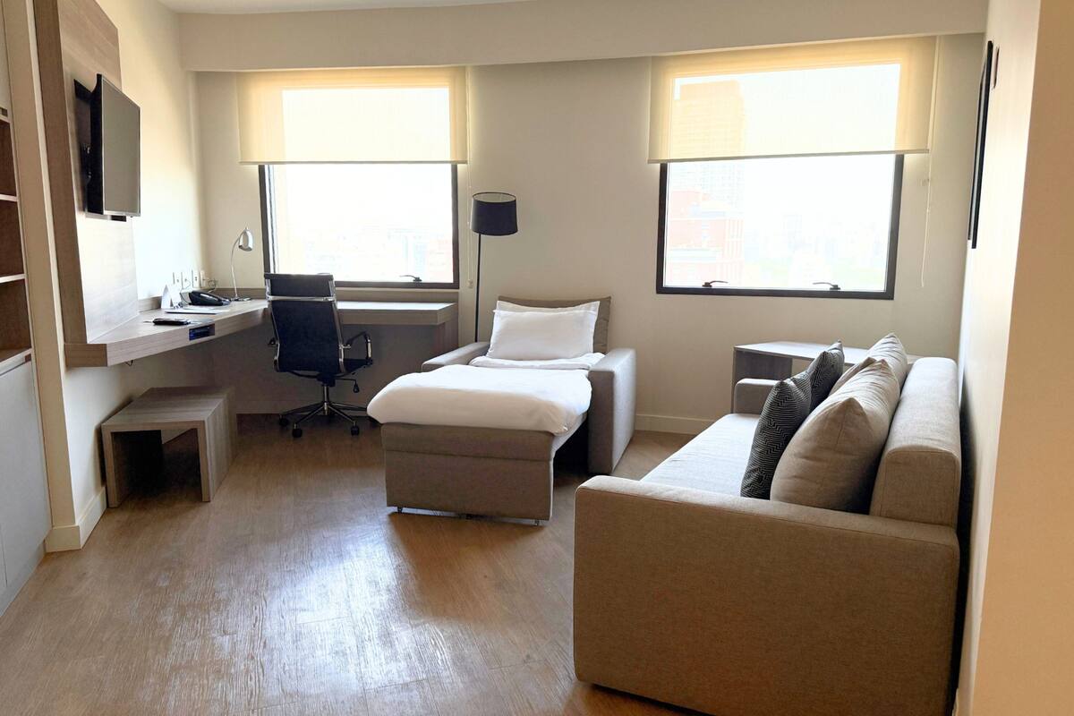 Une chambre d’hôtel moderne équipée d’un lit, d’un bureau, d’une chaise, d’un canapé et de deux fenêtres.