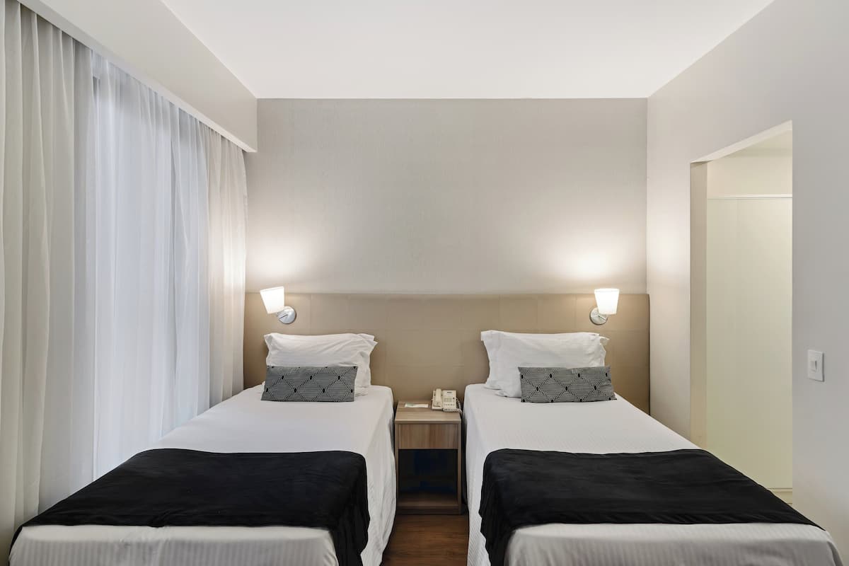 Une chambre d’hôtel avec deux lits, une table de chevet, un téléphone et une fenêtre avec des rideaux.